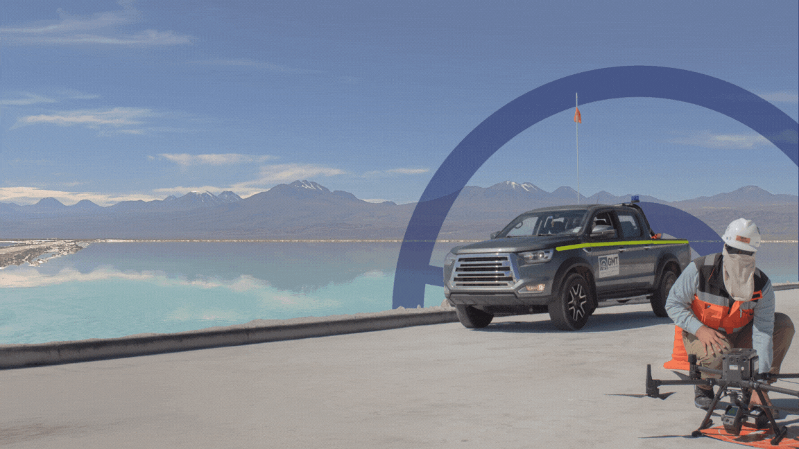 Trabajador de GMT utilizando un drone en un paisaje natural con montañas y agua, junto a un vehículo de la empresa